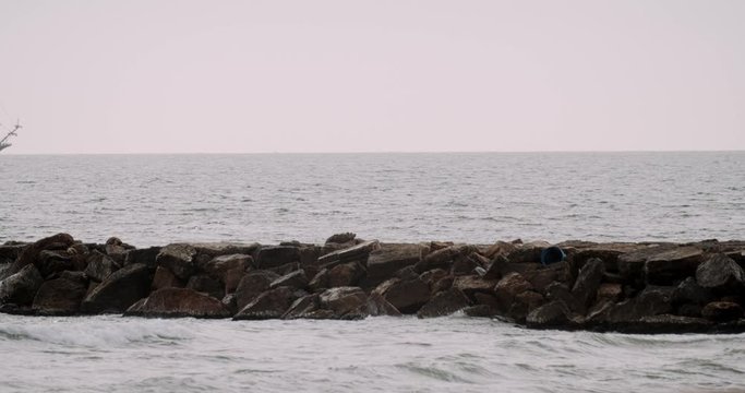 A man walking on a breakwater with a caravel ship replica sailing in the background