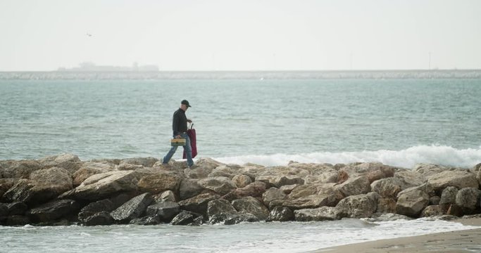 A fisherman walks over a breakwater after fishing on a sunny day in the mediterranean sea
