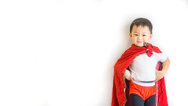 Handsome Little Asian Toddler Boy Jumping Posting From Sofa Couch To Ready To Fight And Fly When He Play As Superhero With Cloak And Red Shot Paint At Home In Living Room.isolated On White Background.