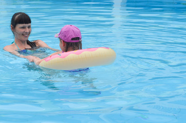 Mother and daughter having fun during the summer vacation. Happy family swimming in the pool