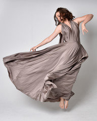  Portrait of a pretty brunette girl wearing a long silver evening gown, full length standing pose...