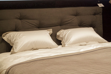 Close-up of new brown-colored blanket with decorative pillows, fabric headboard in bedroom in sample model of hotel or apartment