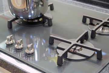 close-up view of the gas ring and control handles of a modern grey glass coocktop