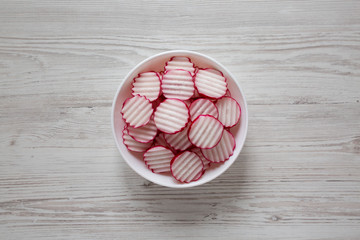 Radish Chips Slices in a white bowl on a white wooden table, top view. Flat lay, overhead, from above.