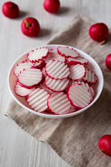 Fresh Radish Chips Slices in a white bowl on a white wooden surface, low angle view. Close-up.