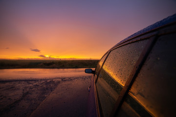 Sunset rain. View next to a car with droplets on the windows.