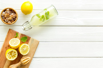 Make lemonade. Drink in bottle near utensil on white wooden background top-down copy space