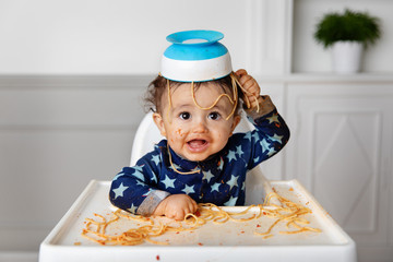 Funny baby with bowl of spaghetti on head