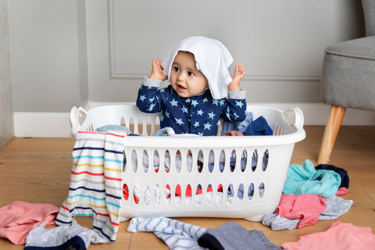 Cute Baby Sitting In Laundry Basket With Clothes On Head