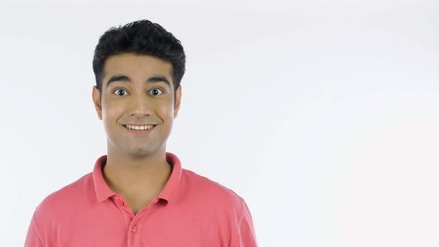 Closeup shot of an Indian guy with surprise or wow expressions - emotions concept. Portrait of a young surprised man standing against the white background and looking at the camera - copy space con...