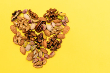 Flat lay ketogenic diet. A mix of walnut,pistachios,pecan,almond are   laid out in the form of heart on the yellow background. Concept of healthy food.Copy space for mock up