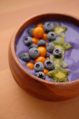 Smoothies of violet color from banana and currant, on top of a blackberry, physalis and kiwi berry. Smoothies in a wooden bowl.