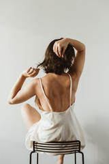 Young beautiful woman in silk underwear sitting on black stool on white background. Sexy fashion...