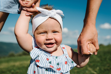 View on baby. Mother, father hold hands daughter enjoy nature and walk in the mountains. Young...