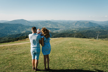 Obraz premium Mom, dad and daughter in the mountains enjoy and look at nature. Back view. Young family spending time together on vacation, outdoors. The concept of family summer holiday.