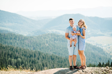 Mom, dad hugging daughter in the mountains enjoy and look at nature. Young family spending time together on vacation, outdoors. The concept of family summer holiday. Mother's, father's, baby's day.