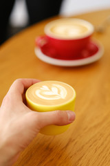 Yellow mug with cappuccino or latte coffee in male hand on a wooden table. Breakfast in the cafe.