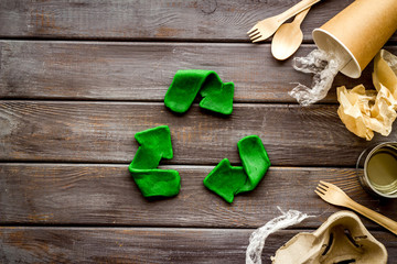 Recycle concept. Green arrows icon among waste on dark wooden background top-down copy space