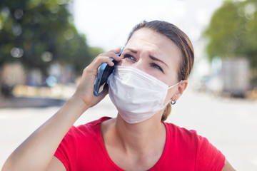 Girl, anxious woman in protective sterile medical mask on her face calling ambulance, need help, talking on cell mobile phone outdoors on asian street. Virus, Chinese pandemic coronavirus concept