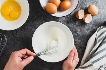 Whipping white eggs with whisk, in a palte. Top view of woman's hands mixing eggs, cooking pastry.