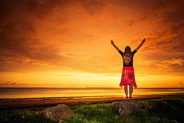 Frau mit rotem Kleid bei Sonnenuntergang am Meer