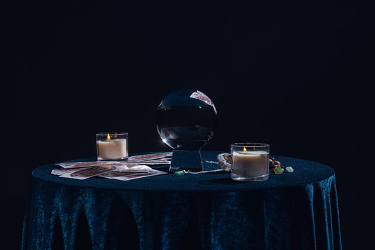 KYIV, UKRAINE - JANUARY 9, 2020: crystal ball with candles, tarot cards, stones and chain on round table isolated on black