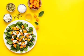 Salad with pumpkin and basil - near ingredients - on yellow background top-down copy space