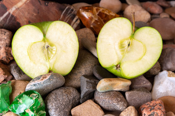 Halves of big green apple lying on pebble decorated with agate, jasper and colored glass