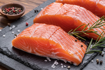 Fresh salmon fillets on black cutting board with herbs and spices.