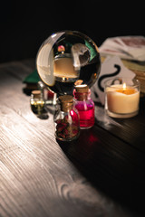 Selective focus of crystal ball, candle and jars of dried herbs and tincture isolated on black