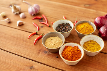food, culinary and eating concept - bowls with different spices, onion, garlic and red hot chili peppers on wooden table