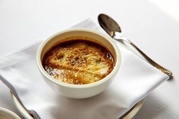 Classic onion soup in a white bowl, standing on a napkin with cutlery close-up 