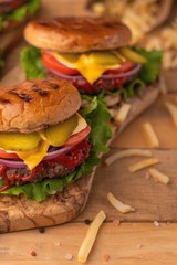 Home or restaurant cuisine. Two fresh large hamburgers with french fries on a wooden background. Vertical photo. Cafe and eateries, restaurant food.