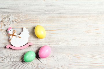 Colored Easter eggs with decorative hen on  light wooden background.