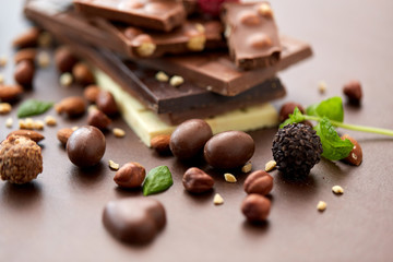 sweets, confectionery and food concept - close up of different chocolate bars, candies and nuts on brown background