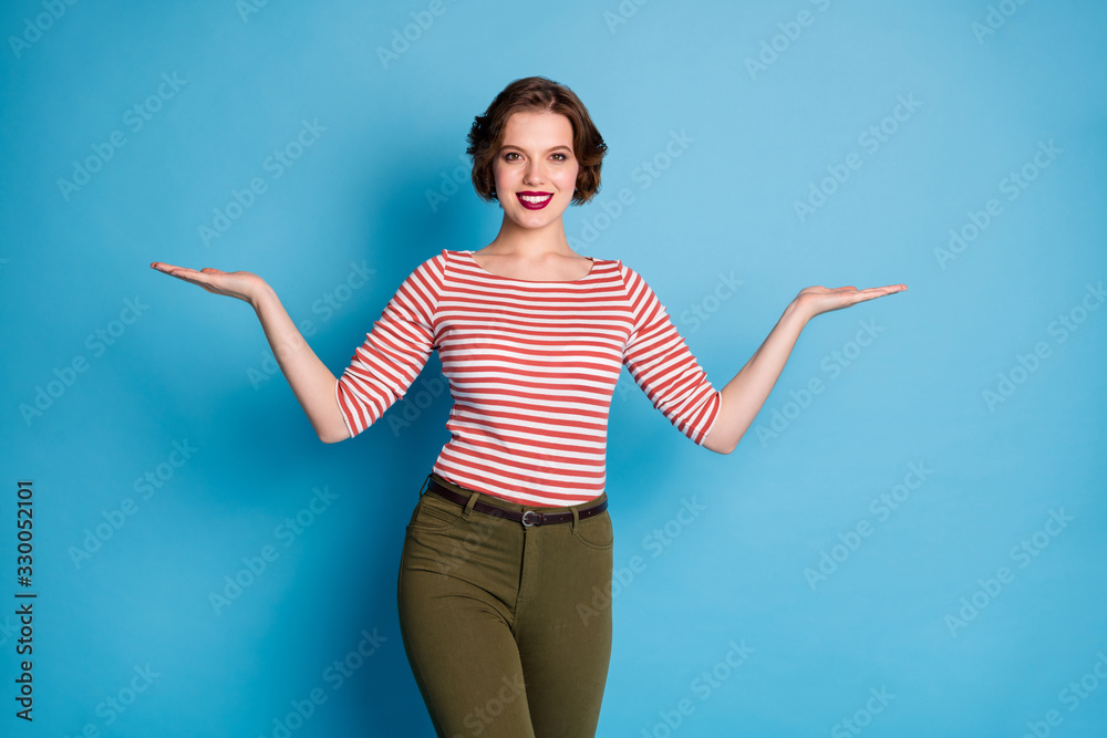 Wall mural Choose one best. Photo of beautiful pretty lady manager hold two open palms presenting low prices products wear casual red white shirt green pants isolated blue color background