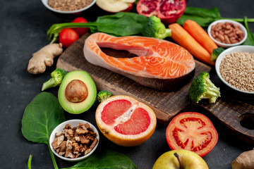 Selection of healthy food: salmon, fruits, seeds, cereals, superfoods, vegetables, leafy vegetables, eggs, rye bread on a stone background