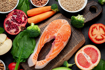 Selection of healthy food: salmon, fruits, seeds, cereals, superfoods, vegetables, leafy vegetables, eggs, rye bread on a stone background