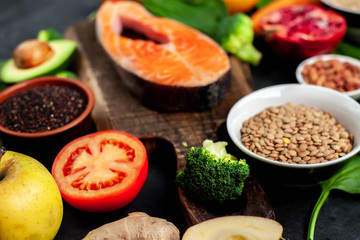 Selection of healthy food: salmon, fruits, seeds, cereals, superfoods, vegetables, leafy vegetables, eggs, rye bread on a stone background
