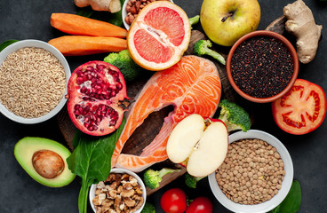 Selection of healthy food: salmon, fruits, seeds, cereals, superfoods, vegetables, leafy vegetables, eggs, rye bread on a stone background