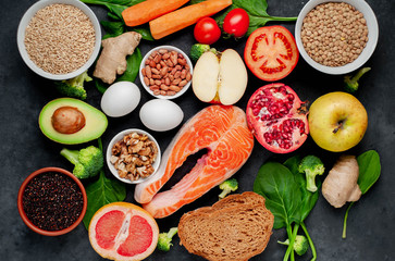 Selection of healthy food: salmon, fruits, seeds, cereals, superfoods, vegetables, leafy vegetables, eggs, rye bread on a stone background