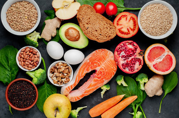 Selection of healthy food: salmon, fruits, seeds, cereals, superfoods, vegetables, leafy vegetables, eggs, rye bread on a stone background