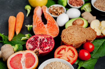 Selection of healthy food: salmon, fruits, seeds, cereals, superfoods, vegetables, leafy vegetables, eggs, rye bread on a stone background