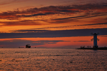 Sunset with silhouettes of tourists at the windmill shaped lighthouse on the Baltic Sea in Swinemünde. Swinoujscie, Poland