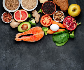 Selection of healthy food: salmon, fruits, seeds, cereals, superfoods, vegetables, leafy vegetables on a stone background   with copy space for your text.Healthy food for people 