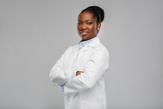 medicine, profession and healthcare concept - smiling african american female doctor or scientist in white coat with crossed hands over grey background