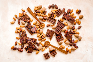 Sweets background with chocolate pieces and nuts on light table top-down