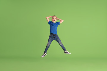 Astonished. Happy boy playing and having fun on green studio background. Caucasian kid in bright cloth looks playful, laughting, smiling. Concept of education, childhood, emotions, facial expression.