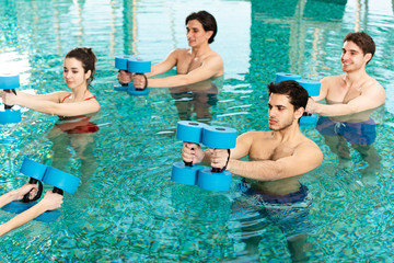 Group of young people exercising with barbells in swimming pool