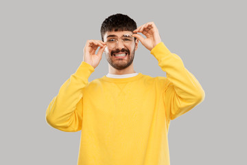 Fototapeta premium vision and people concept - goofy young man in glasses and yellow sweatshirt over grey background